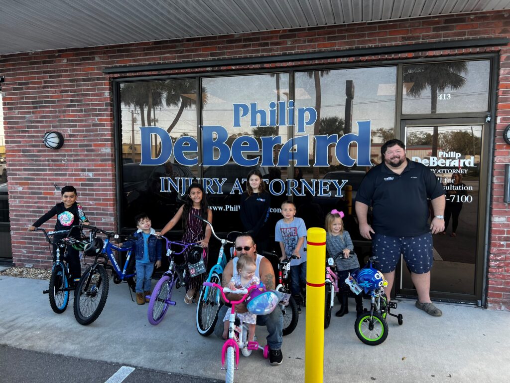 seven children with bikes along with two men in front of a window storefront that says Philip DeBerard Injury Attorney