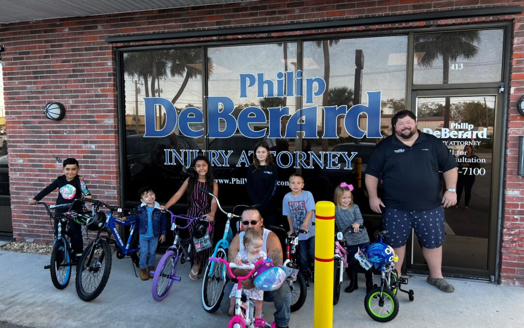 seven children with bikes along with two men in front of a window storefront that says Philip DeBerard Injury Attorney